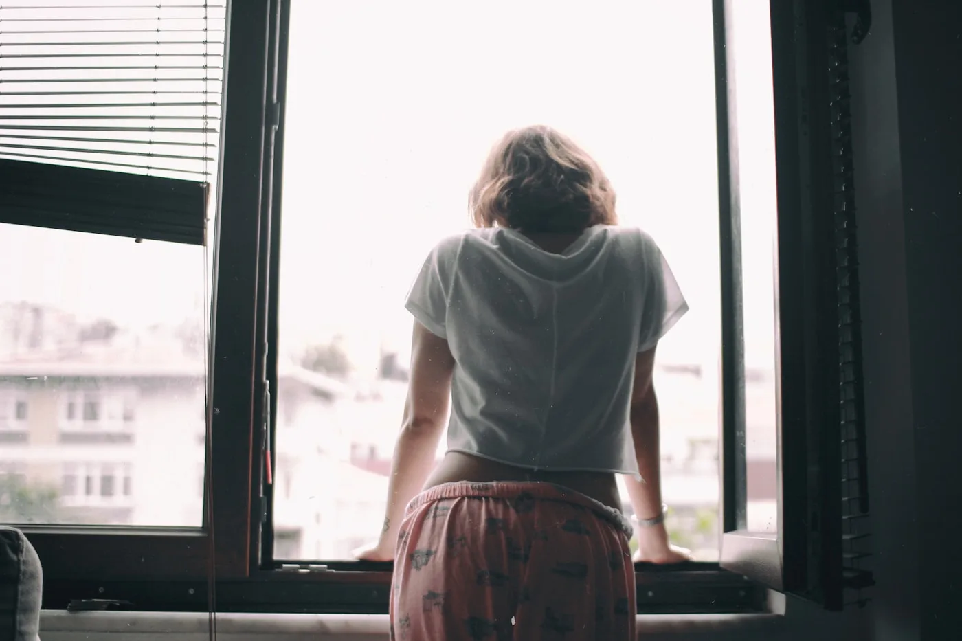 Mujer de espaldas junto a una ventana, en una escena cotidiana de luz natural